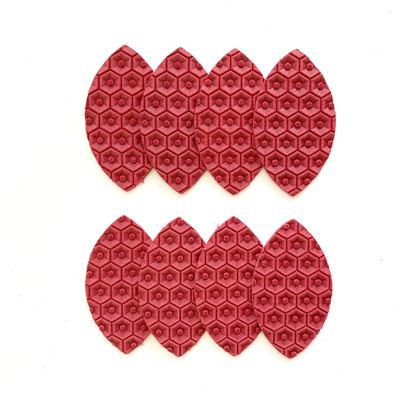 May include: Twelve red leather leaves with a hexagonal pattern. The leaves are arranged in two rows of six.