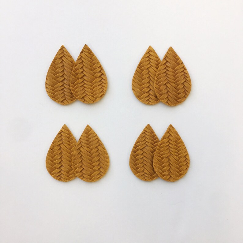 May include: Four pairs of teardrop-shaped earrings in a warm, golden-brown hue. Each earring has a woven, textured design, creating a braided appearance. The earrings are arranged on a white background, showcasing their intricate details.