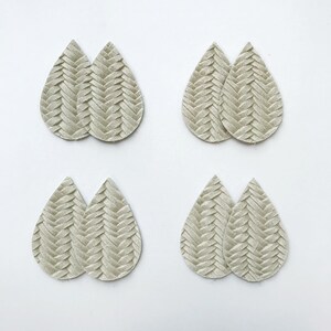 May include: Eight teardrop-shaped earring blanks in a neutral, light grey colour. Each pair features a woven, textured pattern. The earrings are arranged on a white surface, providing a clean and simple presentation for crafting or jewellery making.