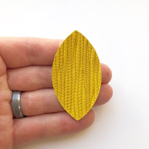 May include: A yellow leather leaf with a textured pattern. The leaf is approximately 5 cm long and 2.5 cm wide.