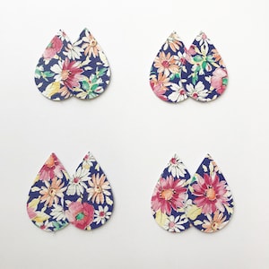 Pu&ograve; includere: Quattro paia di orecchini a forma di goccia con stampa floreale su sfondo bianco. Gli orecchini sono in pelle e hanno uno sfondo blu navy con fiori rosa, bianchi e gialli.