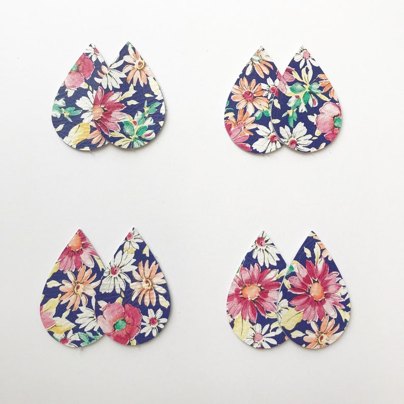 Pu&ograve; includere: Quattro paia di orecchini a forma di goccia con stampa floreale su sfondo bianco. Gli orecchini sono in pelle e hanno uno sfondo blu navy con fiori rosa, bianchi e gialli.