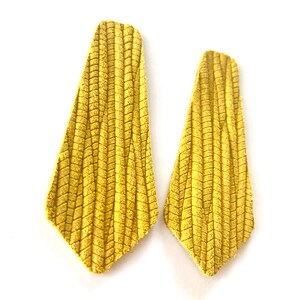 Puede incluir: Un par de pendientes de ante amarillo con un patr&oacute;n de chevron texturizado.