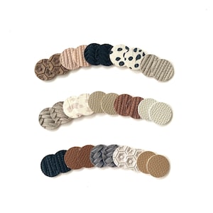 May include: A collection of small, round leather pieces in various colors and textures, arranged in three curved rows against a white background. The pieces showcase embossed patterns, including geometric shapes and animal prints, in shades of brown, beige, and black.