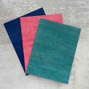 May include: Three sheets of corkboard in different colors: teal, pink, and navy blue. The corkboard has a textured surface.