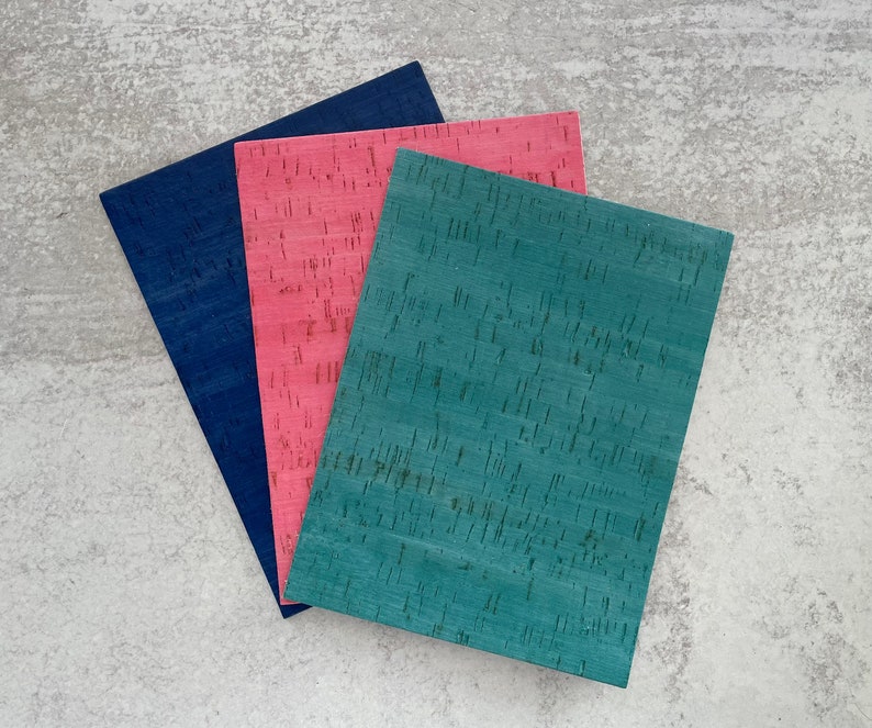 May include: Three sheets of corkboard in different colors: teal, pink, and navy blue. The corkboard has a textured surface.