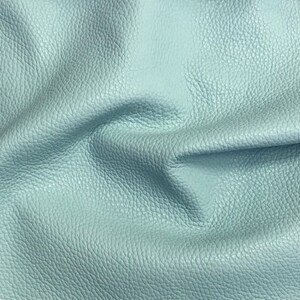 May include: A close-up of a light blue leather fabric with a textured surface.