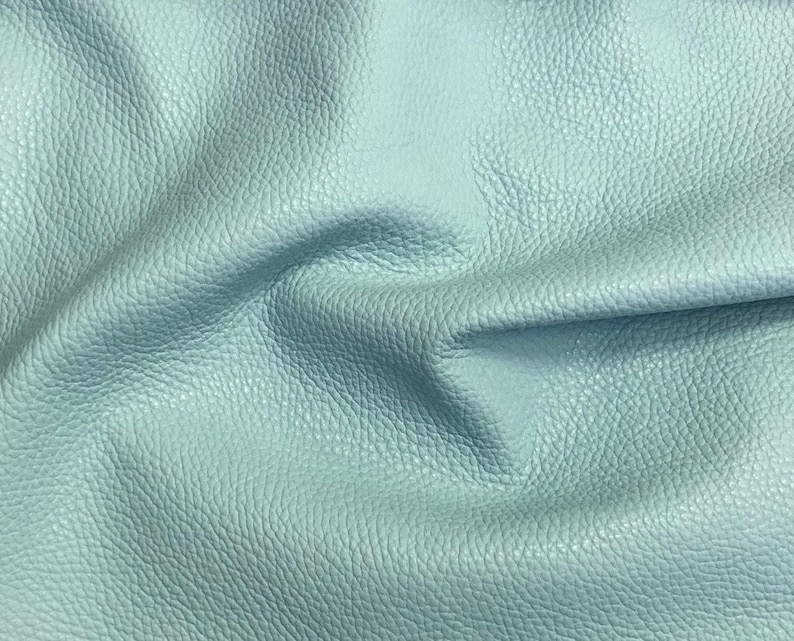 May include: A close-up of a light blue leather fabric with a textured surface.