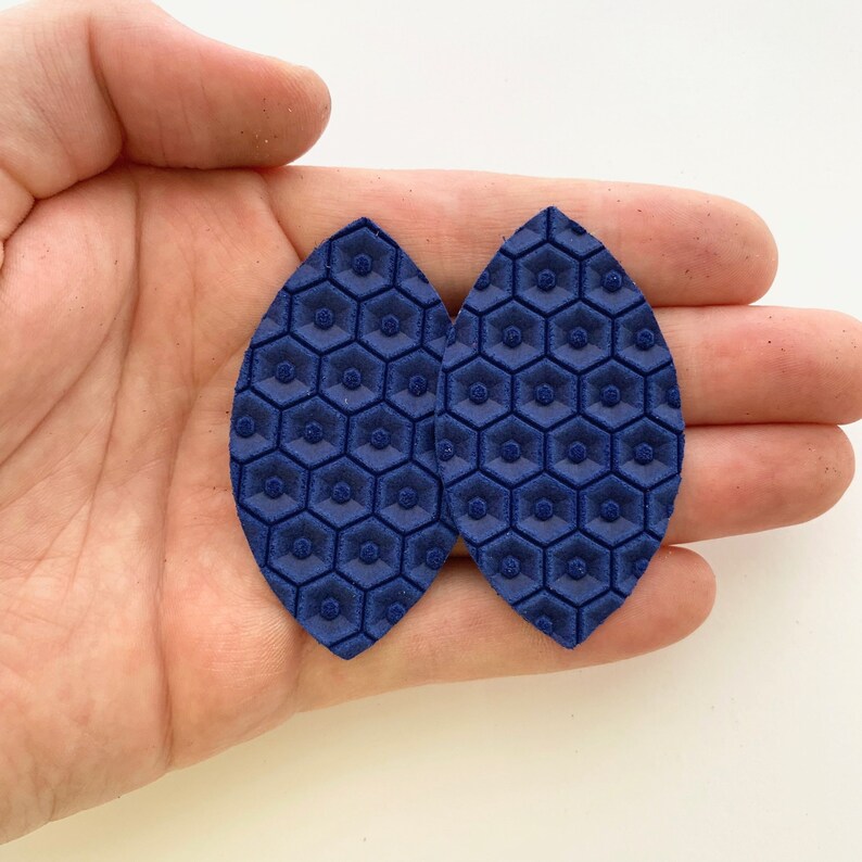 May include: Two navy blue leather earrings with a hexagonal pattern.