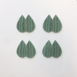 May include: Eight light green teardrop earrings, arranged in pairs. Each earring has a woven or braided texture. The earrings are set against a plain white background. The design of the earrings is the main focus of the image.
