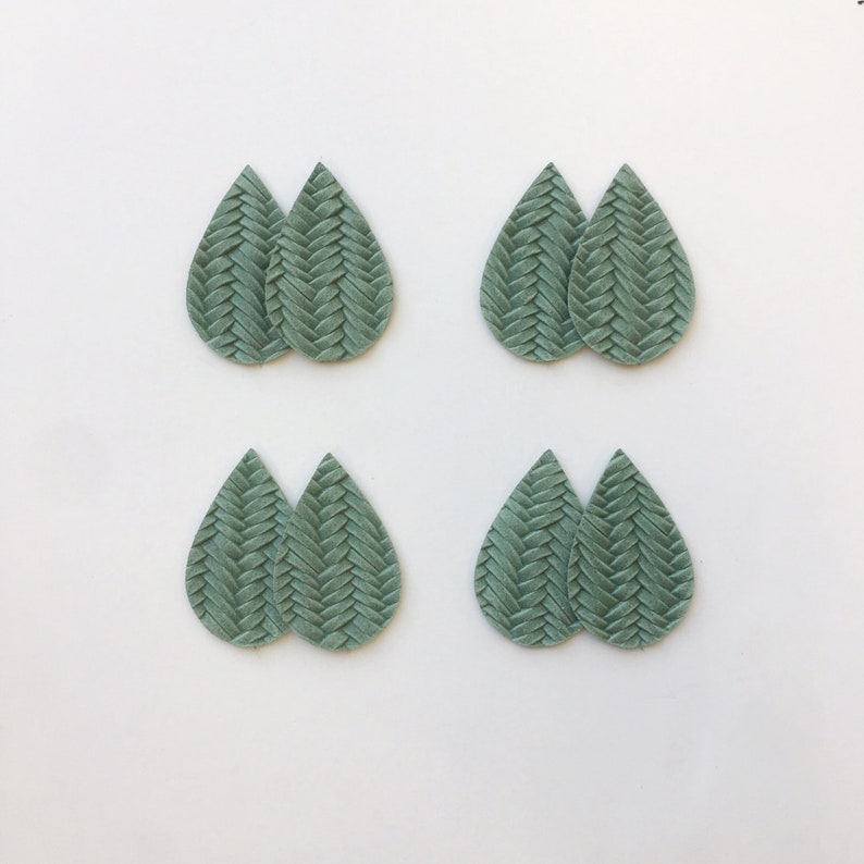 May include: Eight light green teardrop earrings, arranged in pairs. Each earring has a woven or braided texture. The earrings are set against a plain white background. The design of the earrings is the main focus of the image.