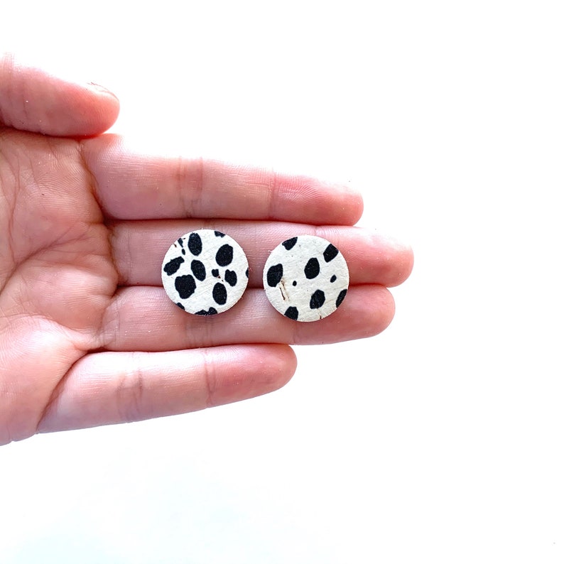May include: A pair of round, white earrings with a black dalmatian spot pattern.