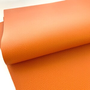 May include: A close-up of a sheet of orange faux leather with a textured surface.