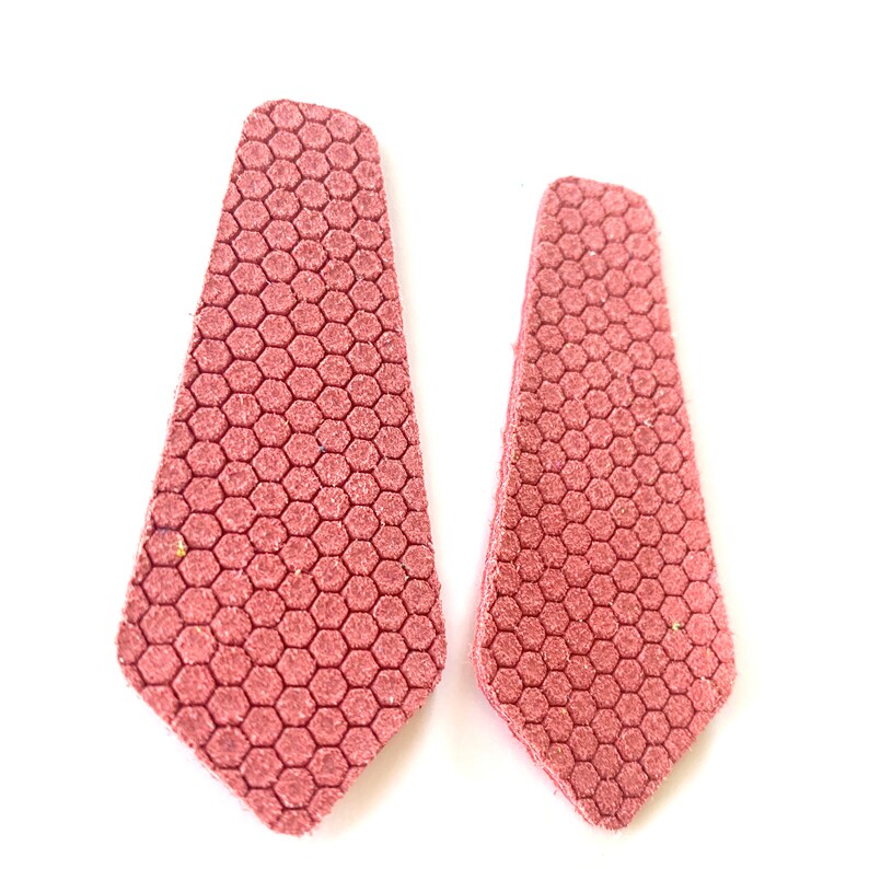 Puede incluir: Un par de pendientes de cuero rosa en forma de corbata con un patr&oacute;n de panal.