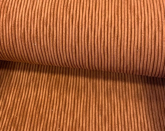 Puede incluir: Primer plano de una tela de pana marrón con textura acanalada. La tela está doblada por la mitad, mostrando el revés del material.
