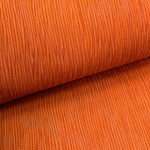 May include: Close-up of a textured orange fabric with a ribbed pattern. The fabric is folded in half, showing the texture on both sides.