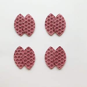 May include: Four pairs of pink leather earrings with a honeycomb pattern. Each earring is shaped like a teardrop.
