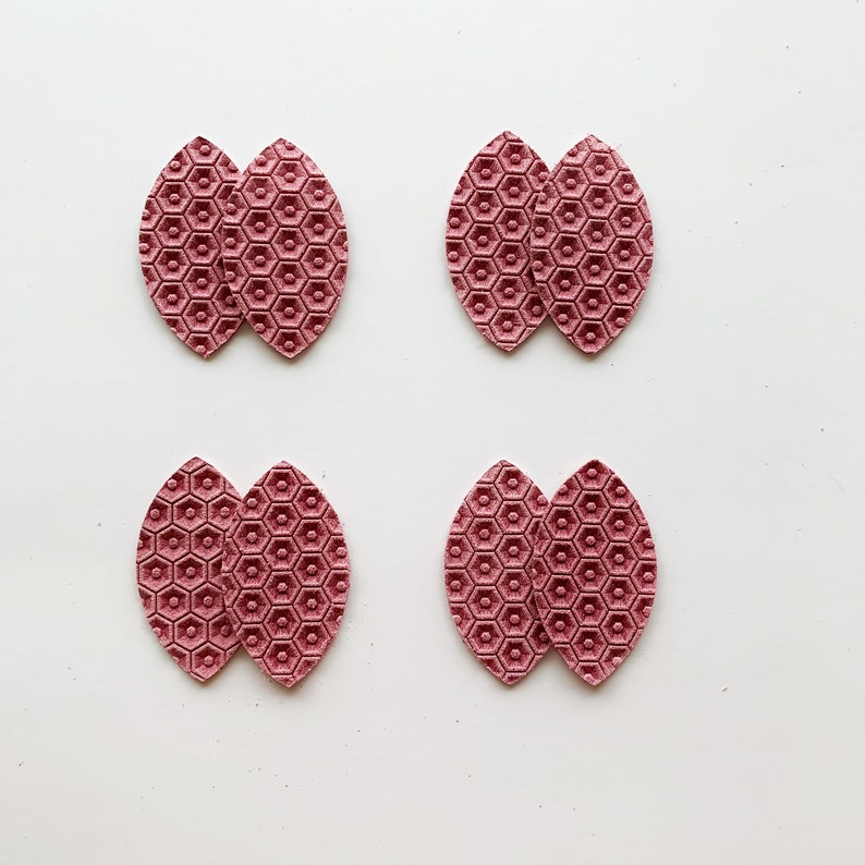 May include: Four pairs of pink leather earrings with a honeycomb pattern. Each earring is shaped like a teardrop.