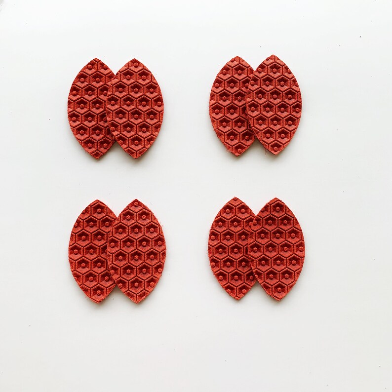 May include: Four pairs of red leather earrings with a honeycomb pattern. Each earring is made of two pieces of leather that are joined together.