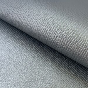 May include: Close-up of a gray textured fabric with a subtle sheen. The fabric has a pebbled or grainy texture.