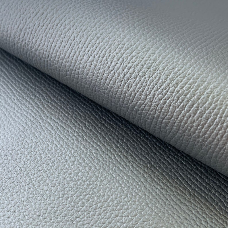 May include: Close-up of a gray textured fabric with a subtle sheen. The fabric has a pebbled or grainy texture.