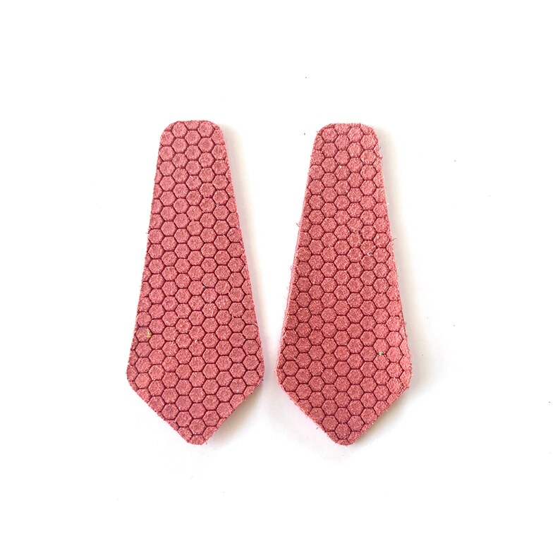 Puede incluir: Un par de pendientes de cuero rosa con un patr&oacute;n hexagonal. Los pendientes tienen forma de l&aacute;grima.