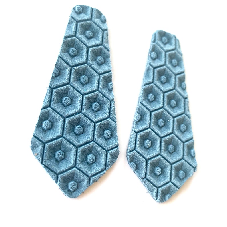 Puede incluir: Un par de pendientes azules con estampado geom&eacute;trico. Los pendientes est&aacute;n hechos de cuero y tienen un patr&oacute;n hexagonal.