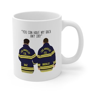May include: White ceramic mug featuring an illustration of two firefighters in navy blue jackets with yellow stripes. The text "YOU CAN HAVE MY BACK ANY DAY" is printed above the figures. The names "DIAZ" and "BUCKLEY" are printed below the figures.