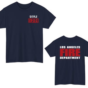 May include: Two navy blue t-shirts. The first t-shirt has "DIAZ 9-1-1" printed on the front in white text with a red rectangle around the text. The second t-shirt has "LOS ANGELES FIRE DEPARTMENT" printed on the front in white text with "FIRE" in red text.