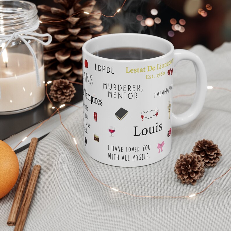 K&ouml;nnte beinhalten: Wei&szlig;e Keramik-Tasse mit schwarzem Kaffee, verziert mit Text und Illustrationen. Die Tasse enth&auml;lt S&auml;tze wie "Murderer, Mentor" und "I have loved you with all myself." Dekorative Elemente sind eine Kerze, Tannenzapfen und Lichterketten.