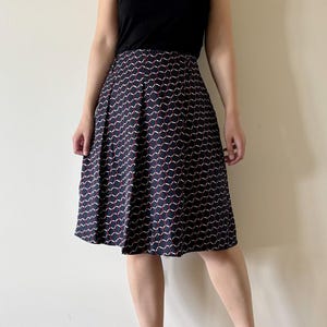 May include: A navy blue knee-length skirt with a repeating pattern of white and red curved lines. The skirt has pleats and is paired with a black top and black heels. The skirt is a classic style.