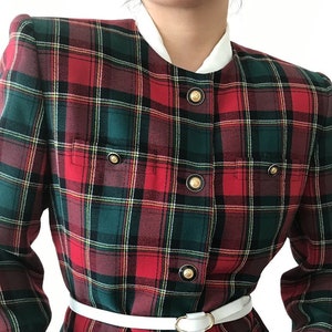 Puede incluir: Una chaqueta de cuadros rojos, verdes y blancos con botones dorados y un cintur&oacute;n blanco.