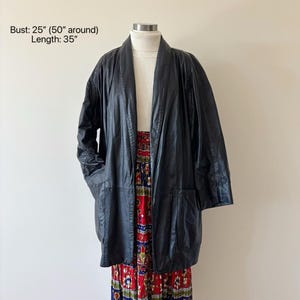 May include: A black leather jacket with a 35-inch length and a 25-inch bust. The jacket has a collarless design and two front pockets. The jacket is displayed over a white turtleneck and a colorful patterned skirt.