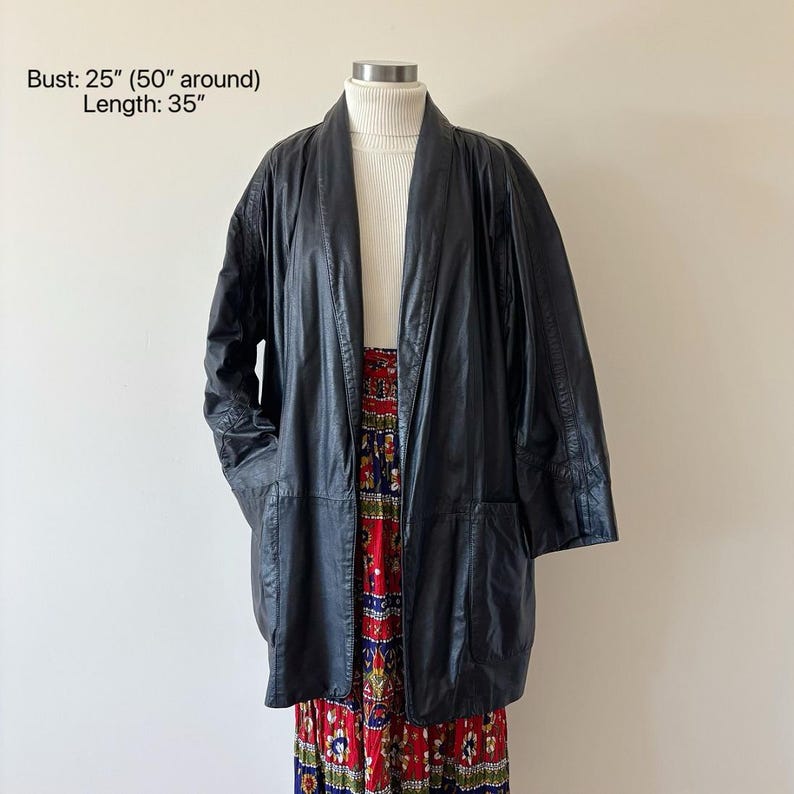 May include: A black leather jacket with a 35-inch length and a 25-inch bust. The jacket has a collarless design and two front pockets. The jacket is displayed over a white turtleneck and a colorful patterned skirt.