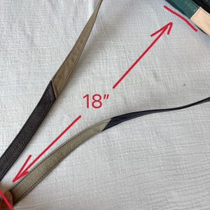 May include: A close-up of a purse strap, measuring 18 inches. The strap is made of leather in shades of black, tan, and cream. The purse itself is visible in the upper right corner, with green, black, and cream panels.