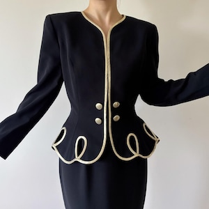 May include: A black blazer featuring a cream-colored piped trim along the open front and a scalloped peplum hem with decorative loops. The jacket includes four round silver-toned buttons arranged in two pairs on the front and long sleeves.