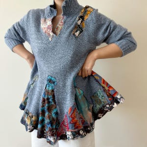 May include: A grey sweater with a high neck and a patchwork design. The sweater has a flared hem with a colourful patchwork design.