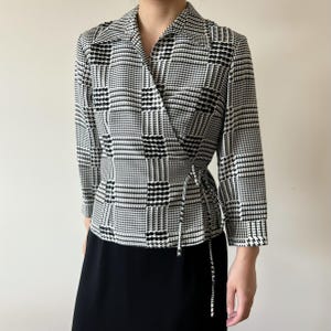 May include: A black and white plaid wrap blouse with a long sleeve and a tie at the waist.
