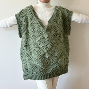 May include: A green crocheted sleeveless vest with a diamond pattern. The vest has a V-neck and is made with a textured stitch.