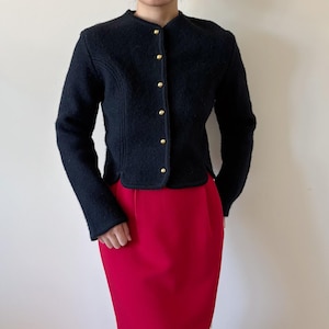 May include: A black wool jacket with a round collar and gold buttons. The jacket is paired with a red pencil skirt. The jacket has long sleeves and a tailored fit. The outfit is suitable for a professional or formal setting.