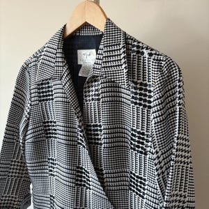 May include: Black and white plaid wrap jacket with a long sleeve and a collar. The jacket has a label that says "V/F/W" on it.