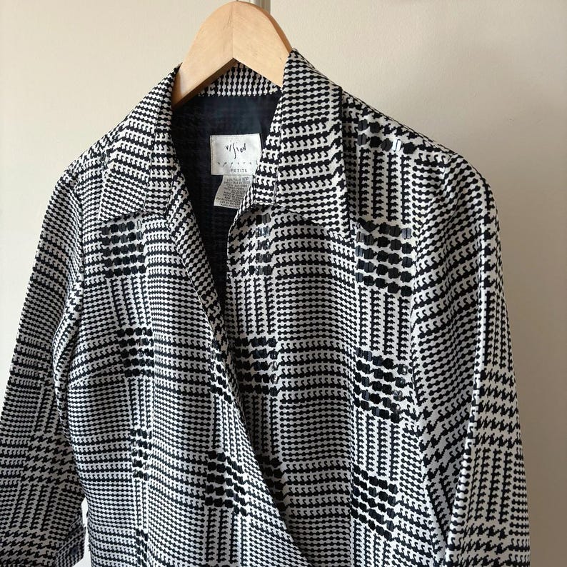 May include: Black and white plaid wrap jacket with a long sleeve and a collar. The jacket has a label that says "V/F/W" on it.