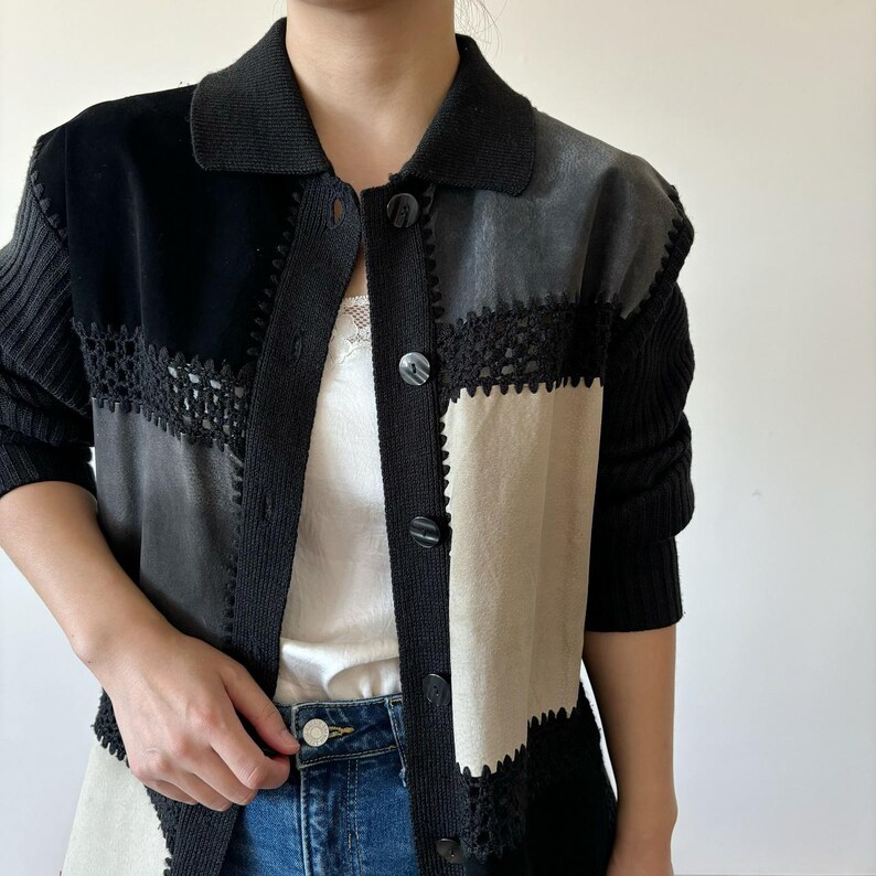 May include: A black, gray, and beige cardigan with crocheted trim and button closures. The cardigan is made of a soft, textured fabric.