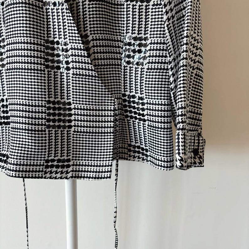 May include: A black and white plaid wrap blouse with long sleeves and a tie at the waist.