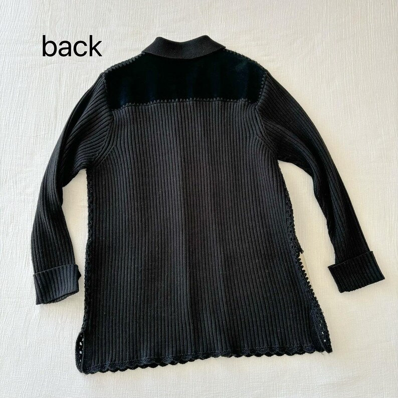 May include: Black ribbed knit cardigan with a black velvet collar and a scalloped hem. The cardigan has a back label that says "back".
