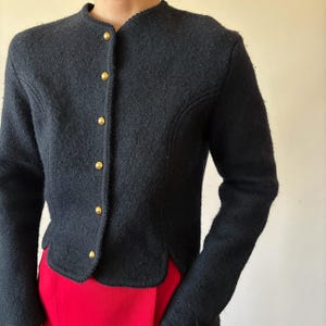 Puede incluir: Chaqueta azul marino oscuro con cuello redondo y mangas largas. La chaqueta presenta botones dorados en la parte delantera y un corte entallado. El dobladillo inferior tiene un dise&ntilde;o festoneado. La chaqueta se combina con una prenda roja.