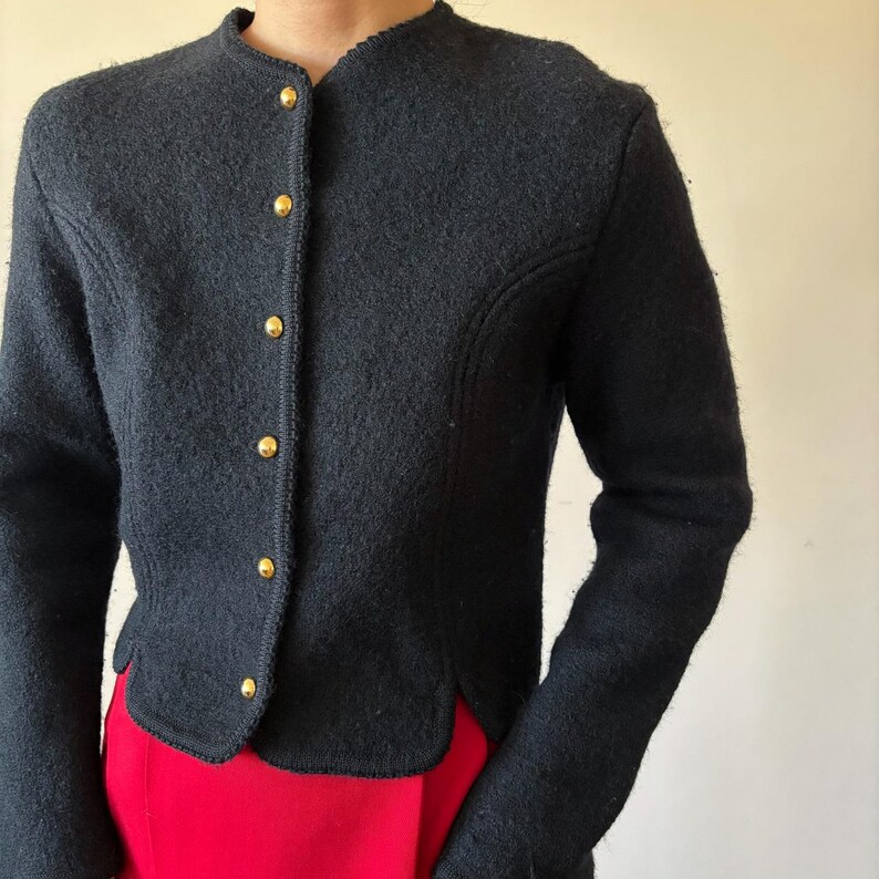 Puede incluir: Chaqueta azul marino oscuro con cuello redondo y mangas largas. La chaqueta presenta botones dorados en la parte delantera y un corte entallado. El dobladillo inferior tiene un dise&ntilde;o festoneado. La chaqueta se combina con una prenda roja.