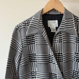 May include: A black and white plaid long-sleeved shirt with a collar and a button closure. The shirt has a 'Vision' label on the front.