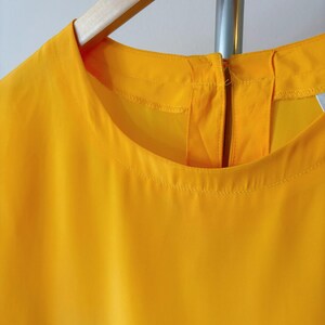 Puede incluir: Una blusa amarilla brillante sin mangas con cuello redondo y cierre de cremallera en la espalda.