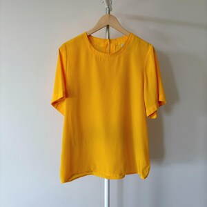 Puede incluir: Una blusa amarilla brillante de manga corta con cuello redondo.